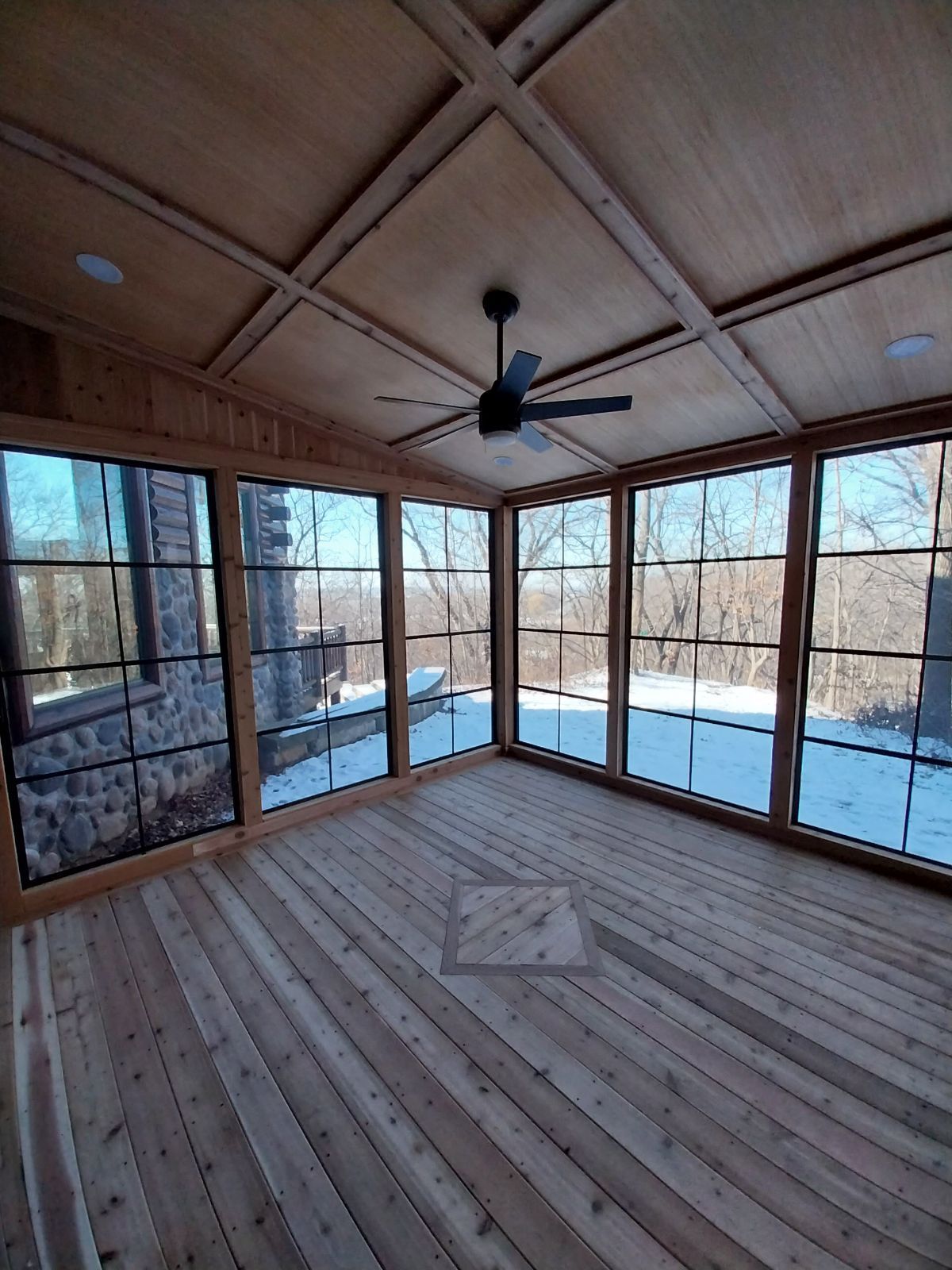 Four-season room interior with cedar floor, coffered wood ceiling and black-framed windows