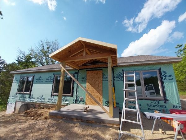 Gabled entry porch framed on a house wrapped for siding