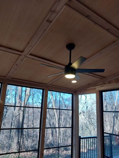 Coffered wood ceiling with a ceiling fan above walls of black-framed windows