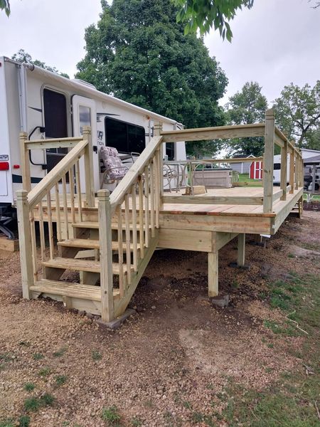 Pressure-treated deck with railings and stairs beside a travel trailer
